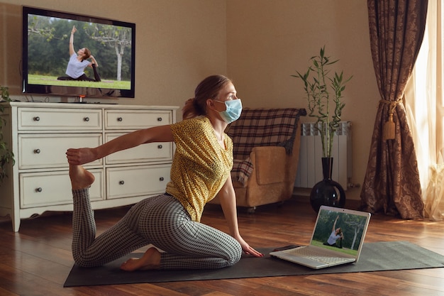 Sporty young woman taking yoga lessons online and practice at home while being quarantine. Concept of healthy lifestyle, wellness, being safe while coronavirus pandemic, looking for new hobby.