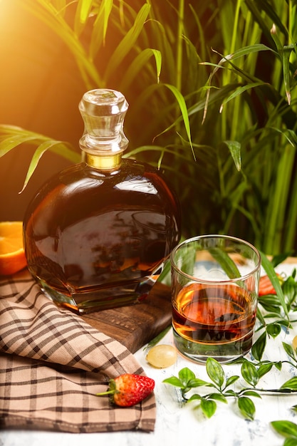 Free photo a spotlight on a crystal glass of brandy with fruits and greenery, shot on a wooden table top