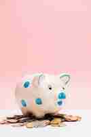 Free photo spotted ceramic piggybank over coins against pink background