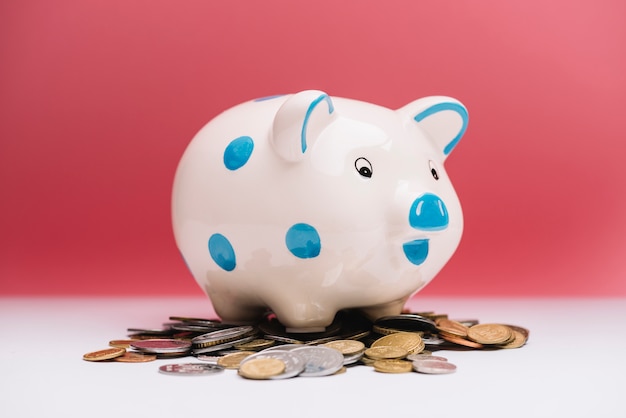 Spotted ceramic piggybank over coins in front of red background
