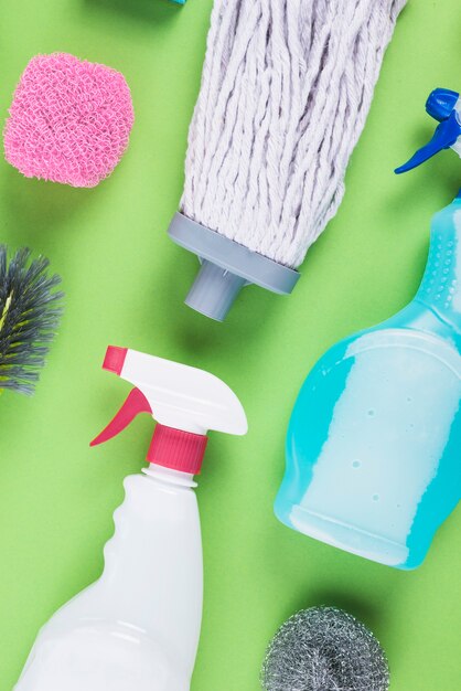 Spray bottles, mop head and scrub on green background