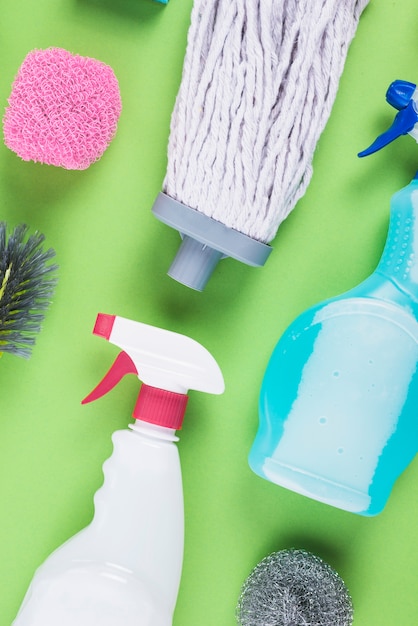 Spray bottles, mop head and scrub on green background