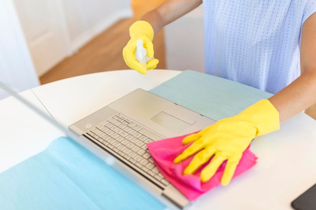 Spraying down wiping and Cleaning laptop Surface with Protective Gloves to disinfect and washing surfaces to protect against the Coronavirus or Covid19