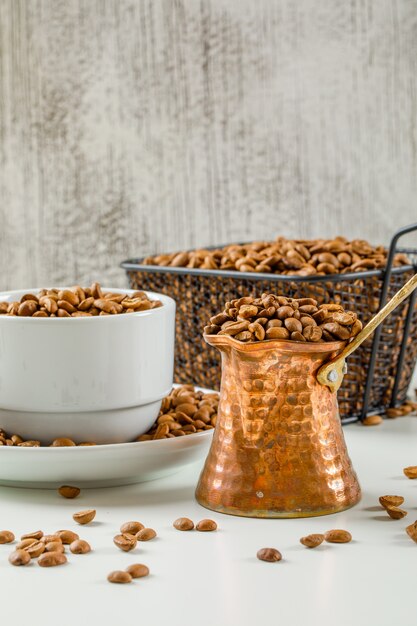 Spread fresh coffee seeds in coffee pot, cup and black colander on a white and grunge wall. side view.