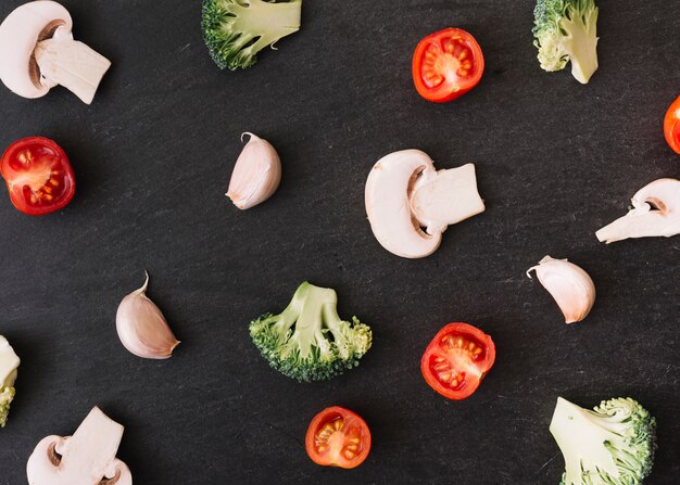 Spread halved mushroom; tomatoes; broccoli and garlic cloves on black surface backdrop