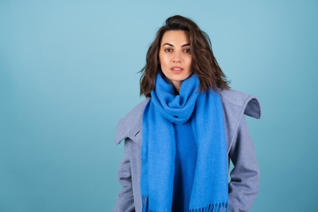 Spring autumn portrait of a woman in a blue knitted sweater, scarf and gray coat, posing fashionably, in anticipation of spring