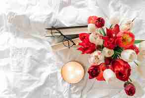 Free photo spring background with a bouquet of tulips a candle and books in a white bed