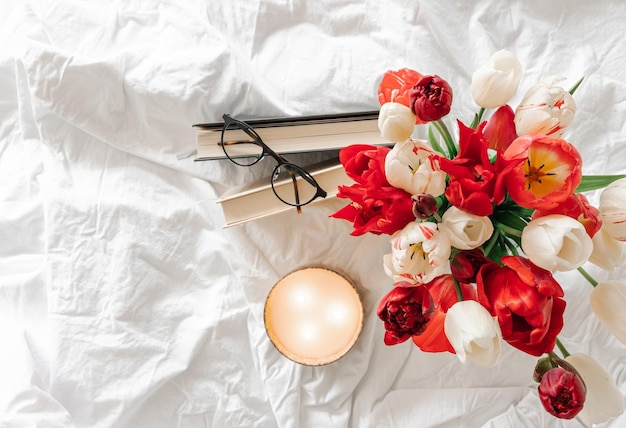 Spring background with a bouquet of tulips a candle and books in a white bed