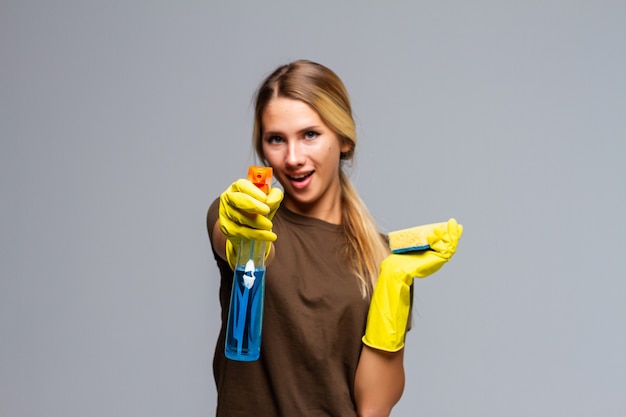 Женщина весенней уборки готова к весенней уборке, улыбаясь с резиновыми перчатками и чистящими средствами. Довольно улыбается молодая женщина, изолированные на белом.