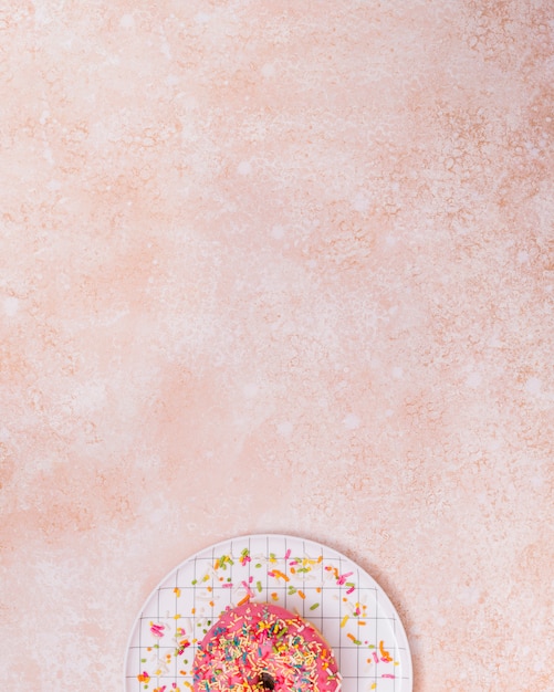 Sprinkles on pink donut over the checkered plate against rustic backdrop with copyspace for writing the text