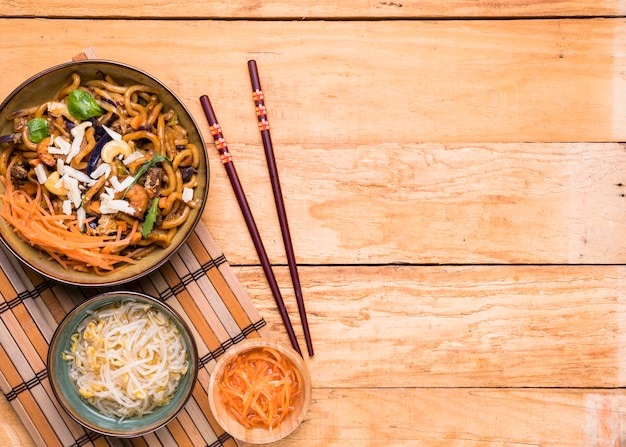 豆をもやします。すりおろしたにんじんと麺と木製のテーブルの上