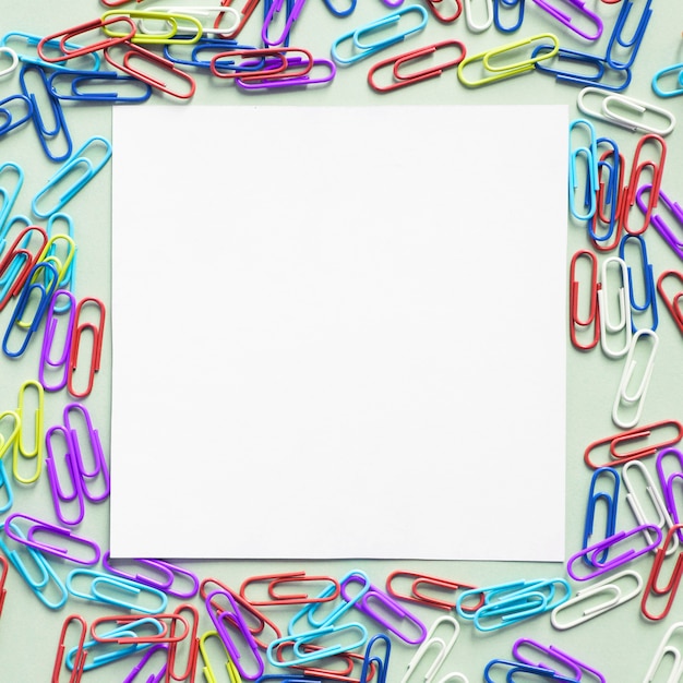 Бесплатное фото Белая картонная бумага квадратной формы, окруженная многими скрепками