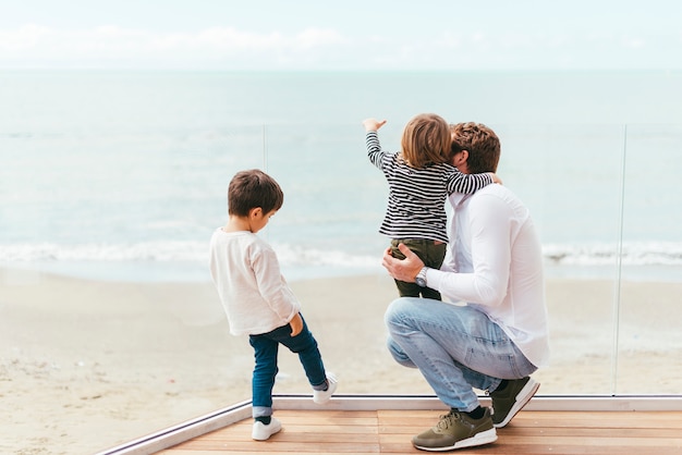 Free photo squatting man holding toddler on seashore