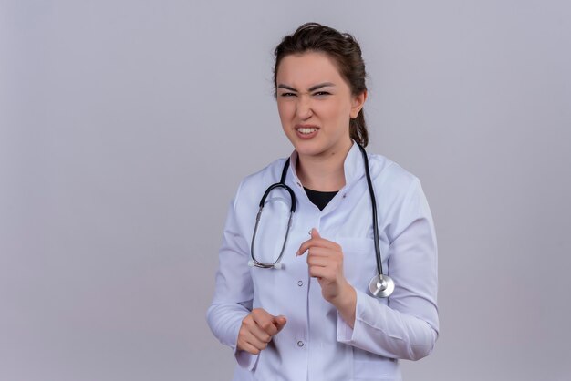 Брезгливая доктор молодая девушка в медицинском халате со стетоскопом на белом фоне
