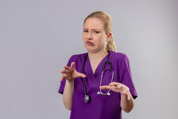 Squeamish doctor young girl wearing purple medical gown and stethoscope on isolated white background