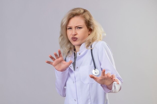 Молодая девушка брезгливая доктор носить стетоскоп в медицинском халате на белом фоне