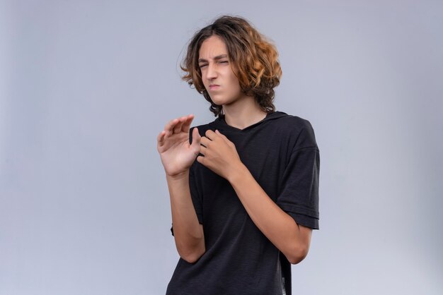 Squeamish guy with long hair in black t-shirt on white background