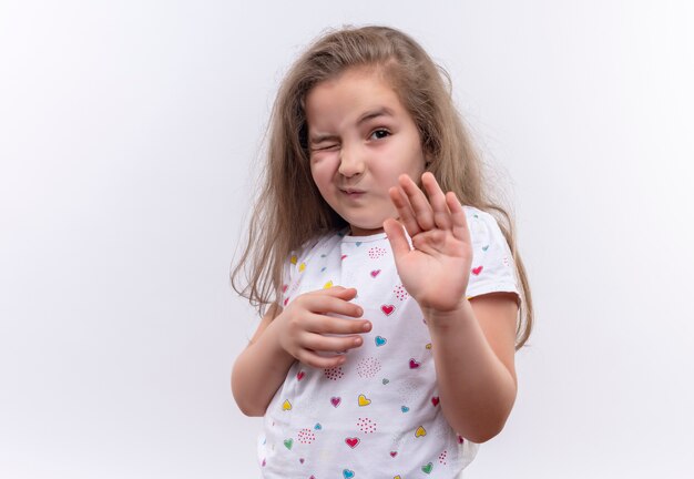 Squeamish little school girl wearing white t-shirt showing stop gesture on isolated white background