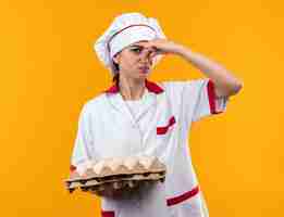 Free photo squeamish young beautiful girl in chef uniform holding batch of eggs closed nose