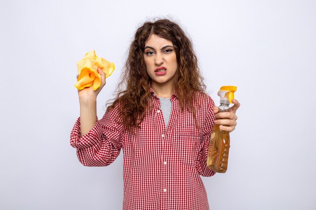 Squeamish young cleaning woman holding cleaning agent with rag