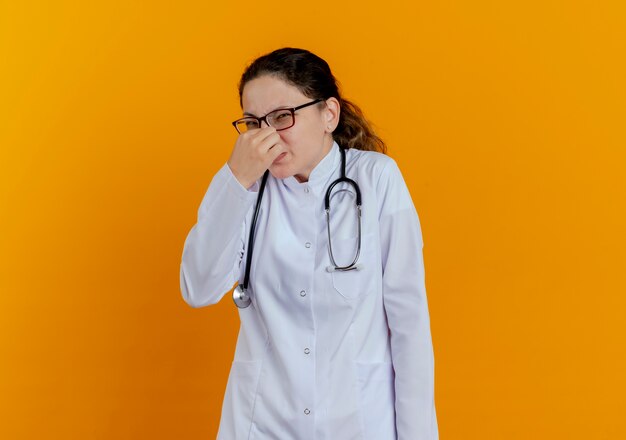 医療用ローブと聴診器を身に着けているきしむ若い女性医師、眼鏡をかけて閉じた鼻を分離
