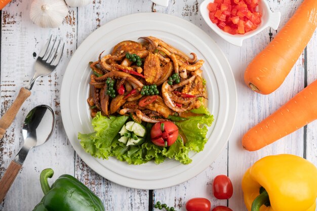 Squid fried with curry paste in white plate, with vegetables and side dishes on a white wooden floor.