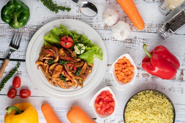 Squid fried with curry paste in white plate, with vegetables and side dishes on a white wooden floor.