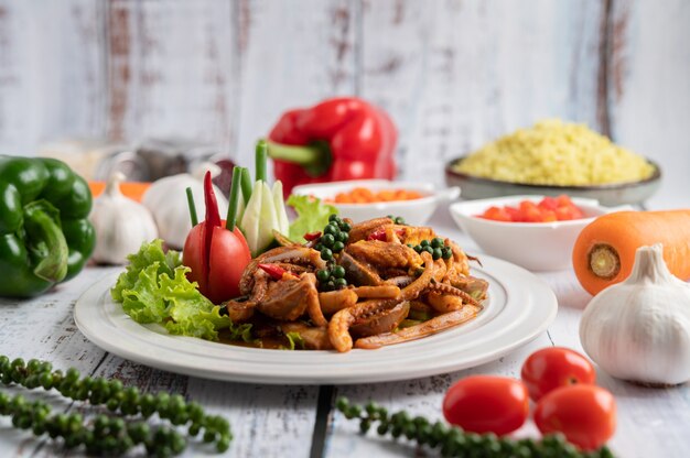 Squid fried with curry paste in white plate, with vegetables and side dishes on a white wooden floor.