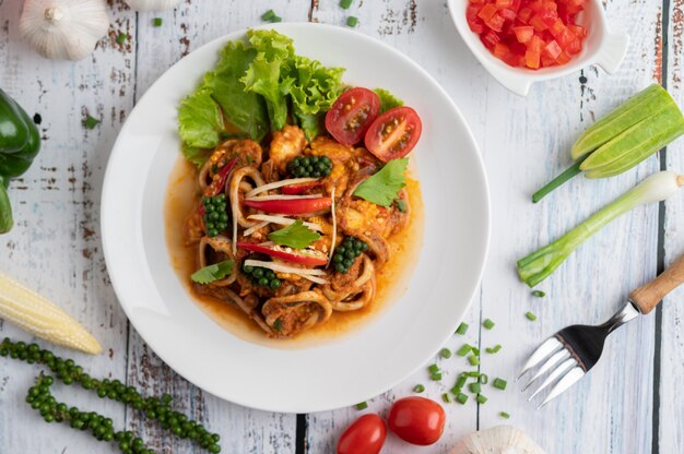 Squid fried with curry paste in white plate, with vegetables and side dishes on a white wooden floor.