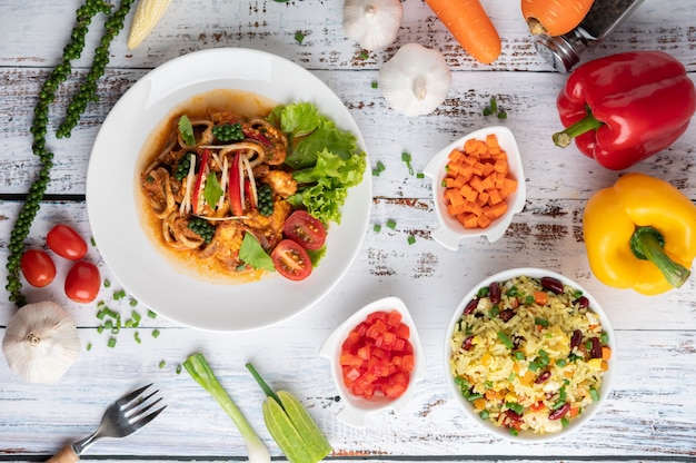 Squid fried with curry paste in white plate, with vegetables and side dishes on a white wooden floor.