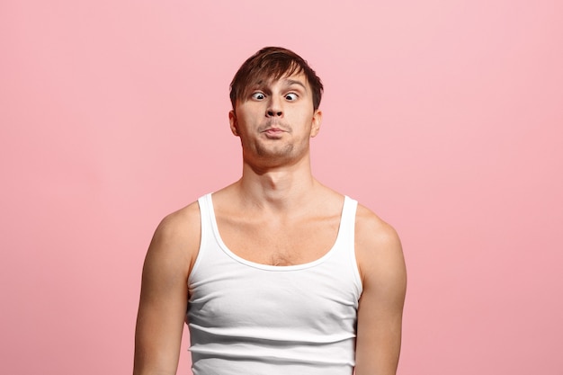 Free photo the squint eyed man with weird expression isolated on pink wall