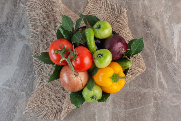 Стек болгарский перец, лук, красные помидоры, зеленые помидоры, огурец, красный лук и листья на куске ткани, на мраморе.