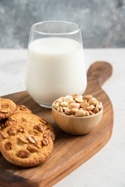 Stack of biscuits with honey, milk and peanuts on wooden board. 