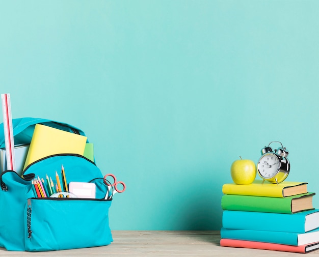Stack of books alarm clock and school backpack with supplies