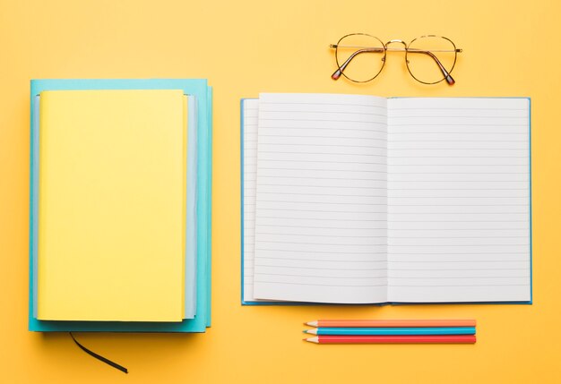 Stack of books and opening blank copybook with arranged pencils 