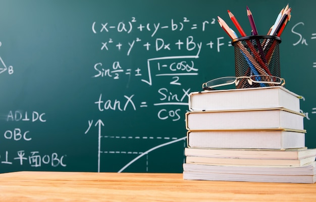 Free photo stack of books with pencil holder and glasses against a chalkboard