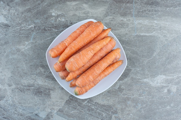 A stack of carrots in the plate , on the marble table. 