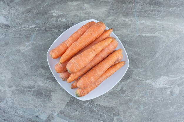 A stack of carrots in the plate , on the marble table. 