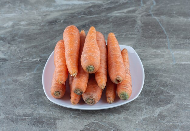 A stack of carrots in the plate , on the marble table. 