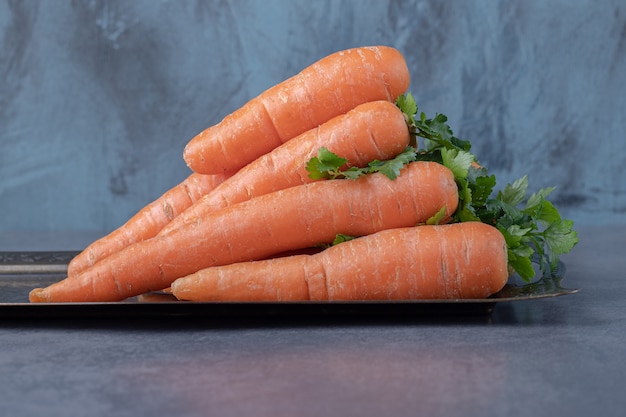 A stack of carrots on the tray , on the marble surface.