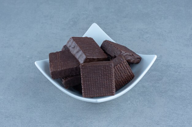 Stack of chocolate wafers in bowl over grey table.