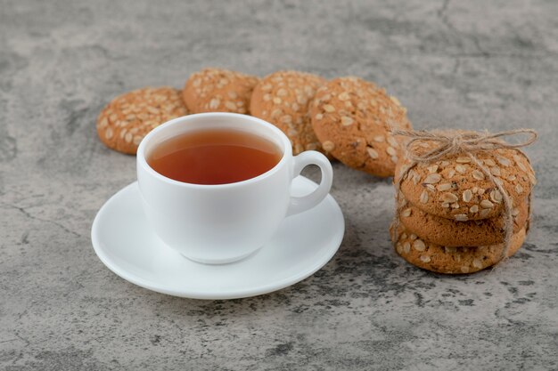 Stack of delicious oatmeal cookies and cup of tea on marble surface.