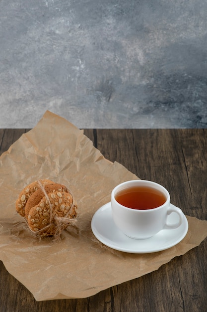 Free photo stack of delicious oatmeal cookies and cup of tea on wooden table.