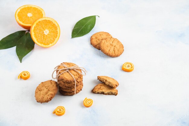 Stack of homemade cookies with orange and leaves on white surface. 