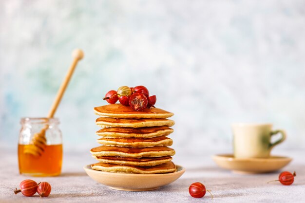 Stack of homemade pancakes with honey syrup and berries.