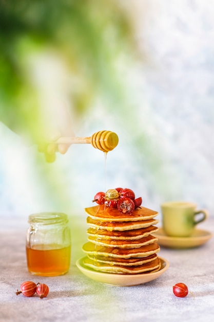 Stack of homemade pancakes with honey syrup and berries.