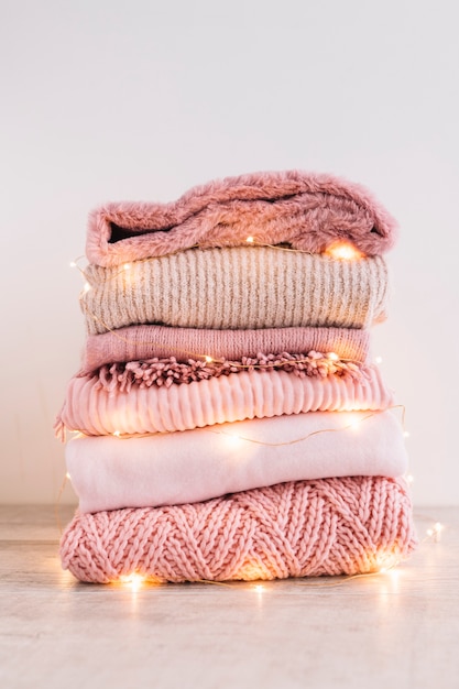 Stack of knitted sweaters with garland on floor