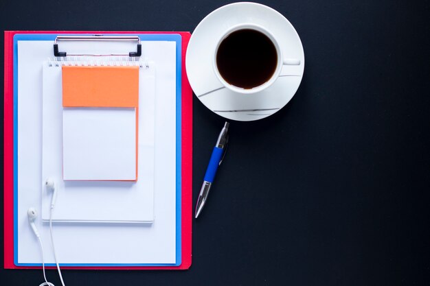 Stack of notebooks and clipboard near pen and coffee