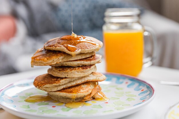 Stack of pancakes with dripping maple syrup and a glass of fresh orange juice