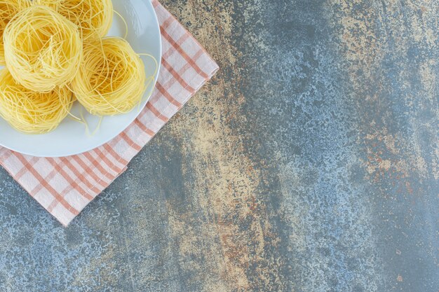 A stack of pasta on the plate on the towel, on the marble background.